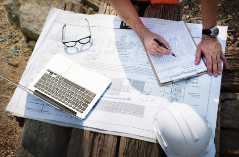 engenheiro trabalhando em cima da planta baixa com notebook