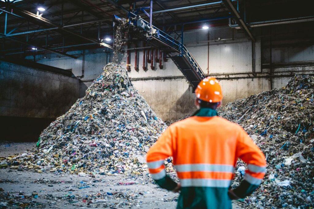 Home 86 Trabalhador de capacete observa pilha de resíduos recicláveis em galpão industrial. Serviços do cadastro de grande gerador de resíduos sólidos da Multilix.