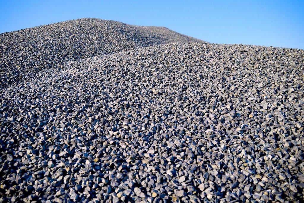 Foto em plano detalhado de uma pilha de Brita Graduada Simples da Multilix, composta por pedras pequenas cinzas e granulometria uniforme, sob céu azul.