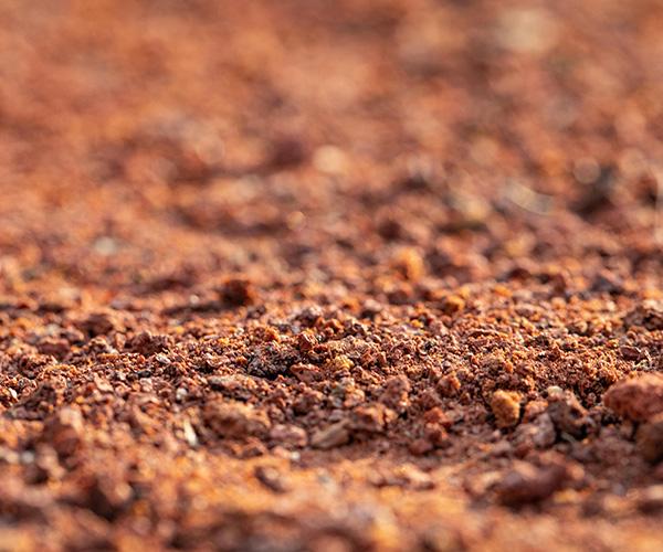 Close-up em textura granulada de terra vermelha para aterro Multilix, mostrando pequenos torrões e detritos orgânicos, ideal para terraplanagem e obras de base.